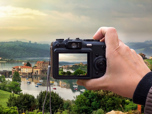 Mano sujetando una cámara digital compacta que toma una foto de un paisaje