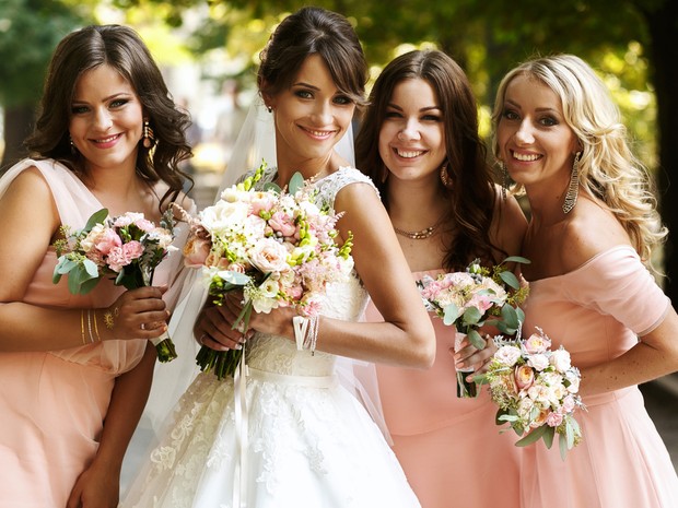 Una mujer joven vestida de novia y sus tres damas de honor con vestidos rosas y ramos de flores en las manos