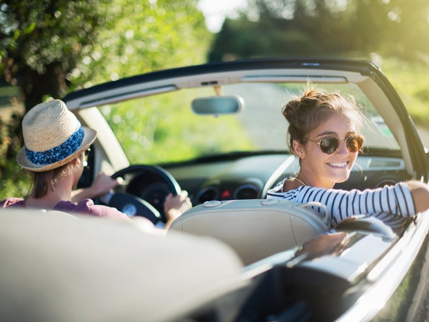 Dos chicas jóvenes en un coche descapotable. La copiloto está mirando hacia atrás sonriendo con unas gafas de sol.