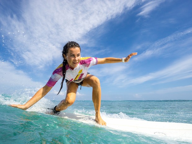 Mujer joven con una coleta larga haciendo surf sobre una tabla blanca