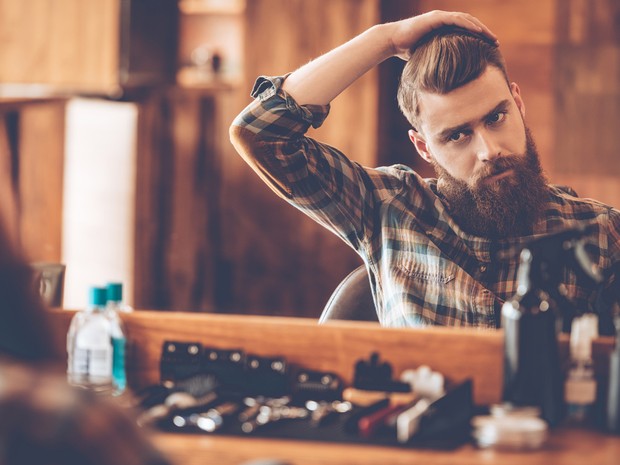 Hombre con barba en una barbería mirándose al espejo