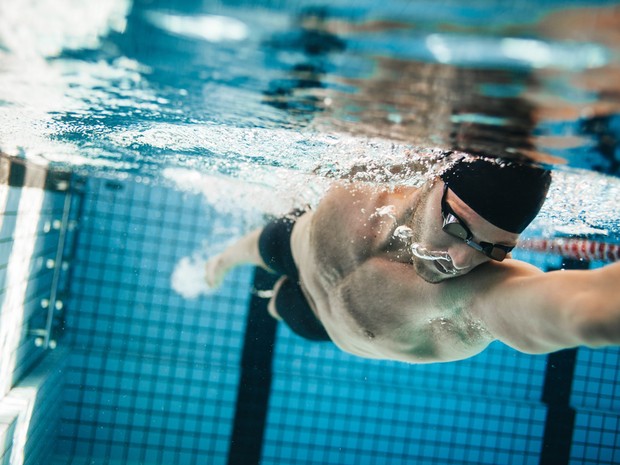Chico joven buceando en una piscina con gorro de piscina, bañador y gafas negras
