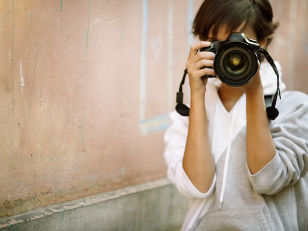 Mujer fotógrafa con una cámara réflex en las manos. Lleva una sudadera gris y blanca.